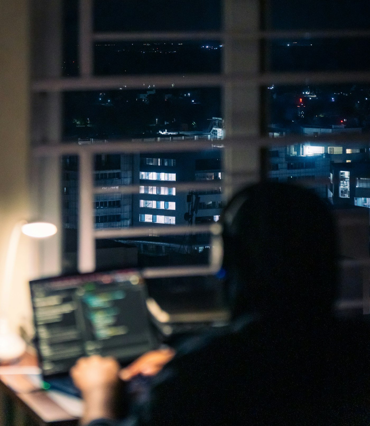 Personne travaillant sur un ordinateur portable de nuit face à la ville